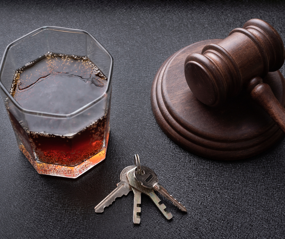 glass of dark liquid with bubbles, a set of keys, and a wooden judge's gavel on a dark surface, symbolizing the connection between drinking, driving, and legal consequences